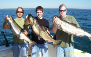 Three men in a Reel Sensation charter boat carrying three large trophy fish from Lake Michigan